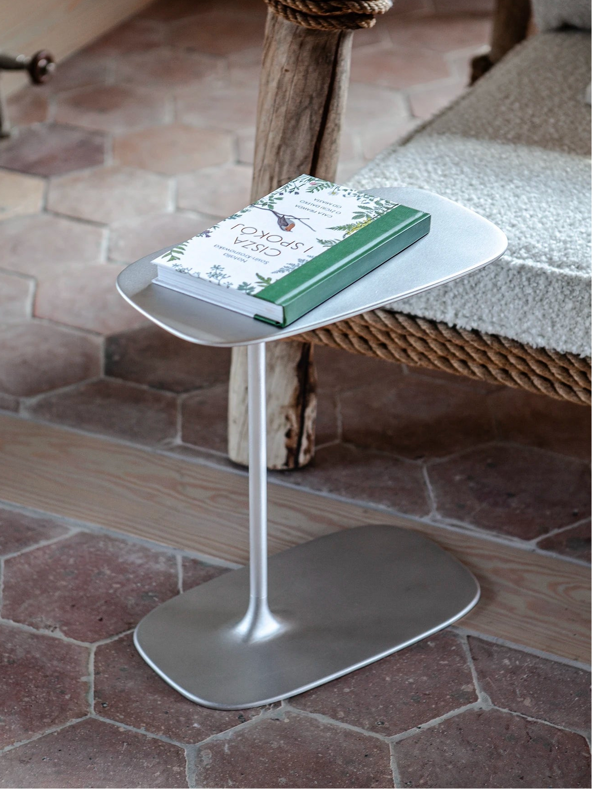 Satin chrome-like c-table styled with a book by a low profile sofa