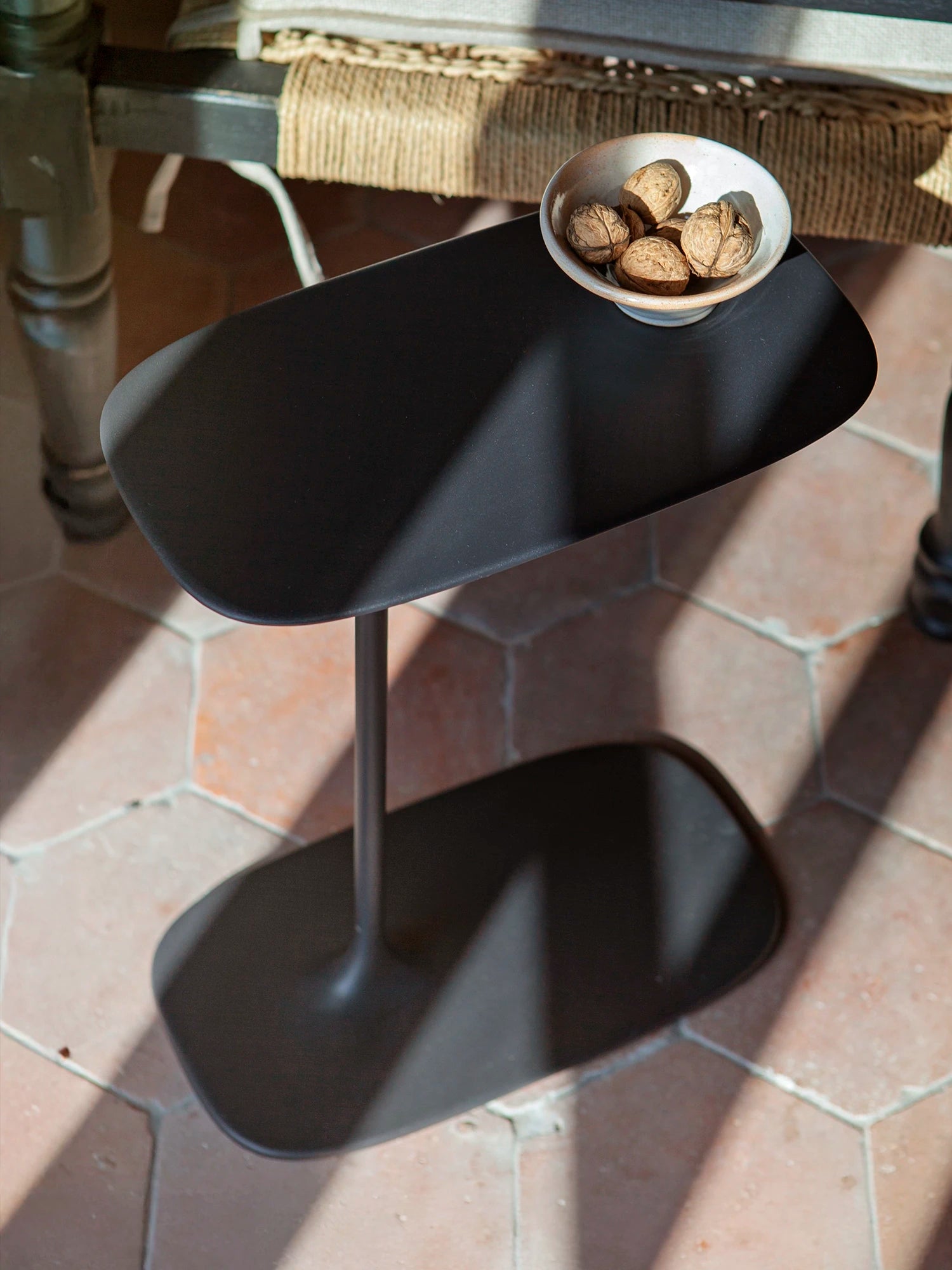 Top view of the black Coated Low table, reflecting a monolithic and seamless metal design. Tabletop styled with bowl of walnuts.