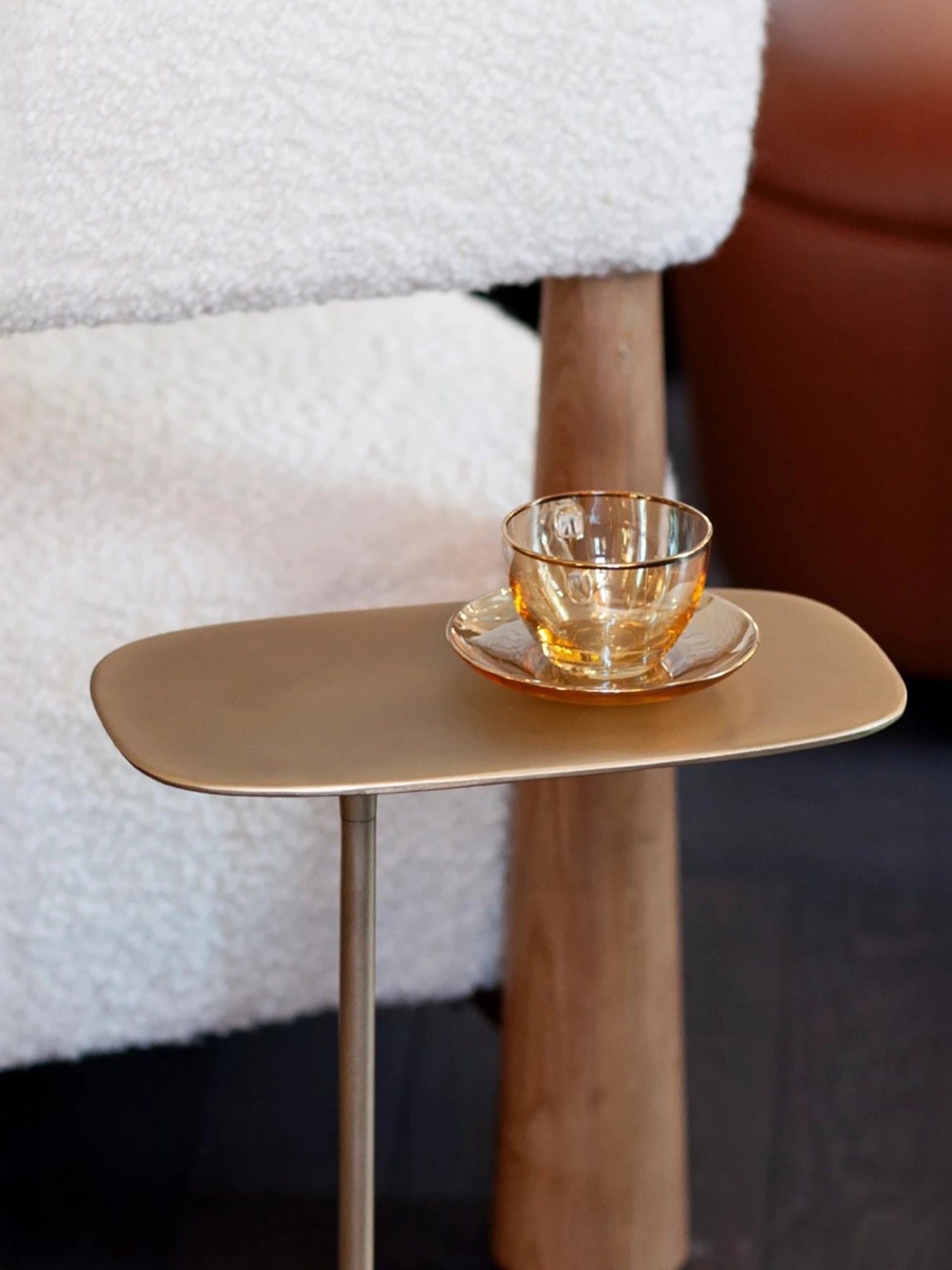 Soft golden reflections on the satin brushed brass surface of a low-profile Fluid table. A glass coffee cup shining on top.